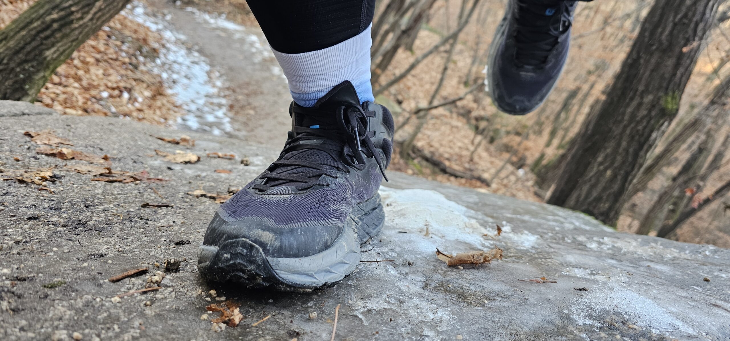 A close-up shot of trail running shoes stepping on a rock with thin ice, highlighting the slippery early-winter terrain on Sapae Mountain.
