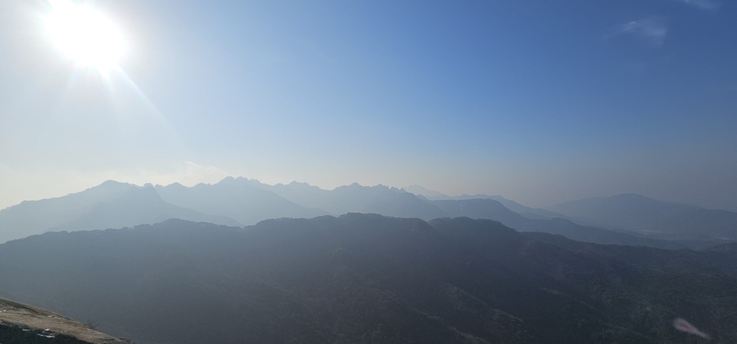 A wide view of layered mountain silhouettes under bright morning sunlight, capturing the peaceful winter atmosphere from Sapae Mountain.